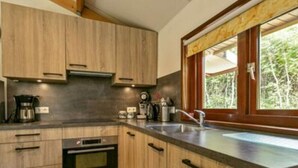 Cozinha moderna com armários de madeira, forno embutido, máquina de café e janela com vista para o verde.