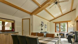 Uma sala de estar ampla com teto alto, vigas de madeira, mesa de jantar com cadeiras, sofá e lareira.