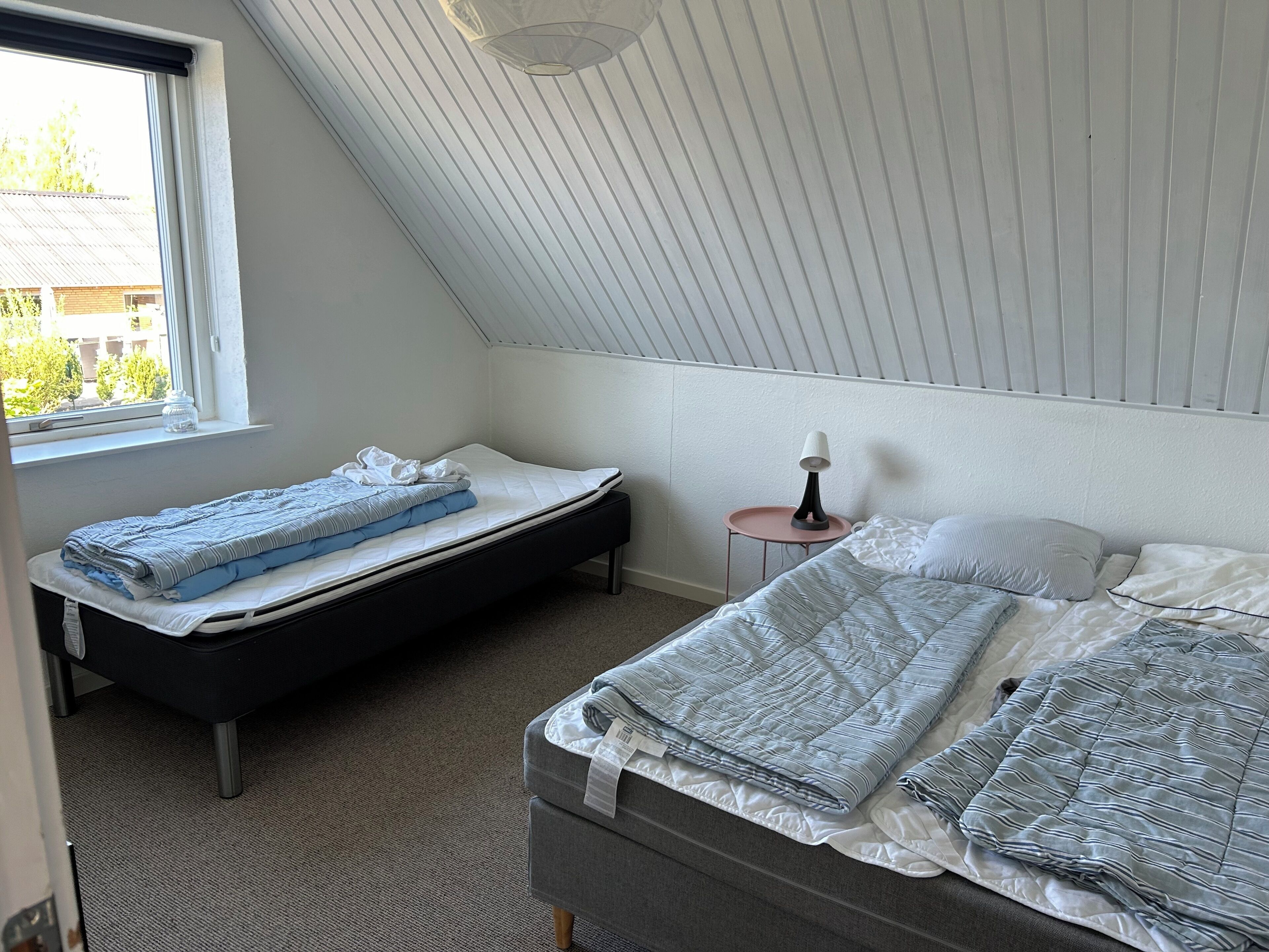 Een slaapkamer met twee bedden, een klein tafeltje met een lamp en een raam met uitzicht op gebouwen en bomen.