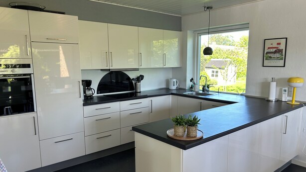 A modern kitchen with white cabinets, a black countertop, and a window providing a view of greenery outside.