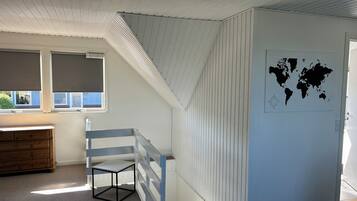 Une pièce avec un plafond en pente, une carte du monde accrochée au mur, une fenêtre avec des stores, une commode en bois et une petite table.