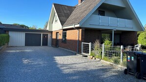 A two-story house with a garage, a gravel driveway, and a fenced area with outdoor seating.