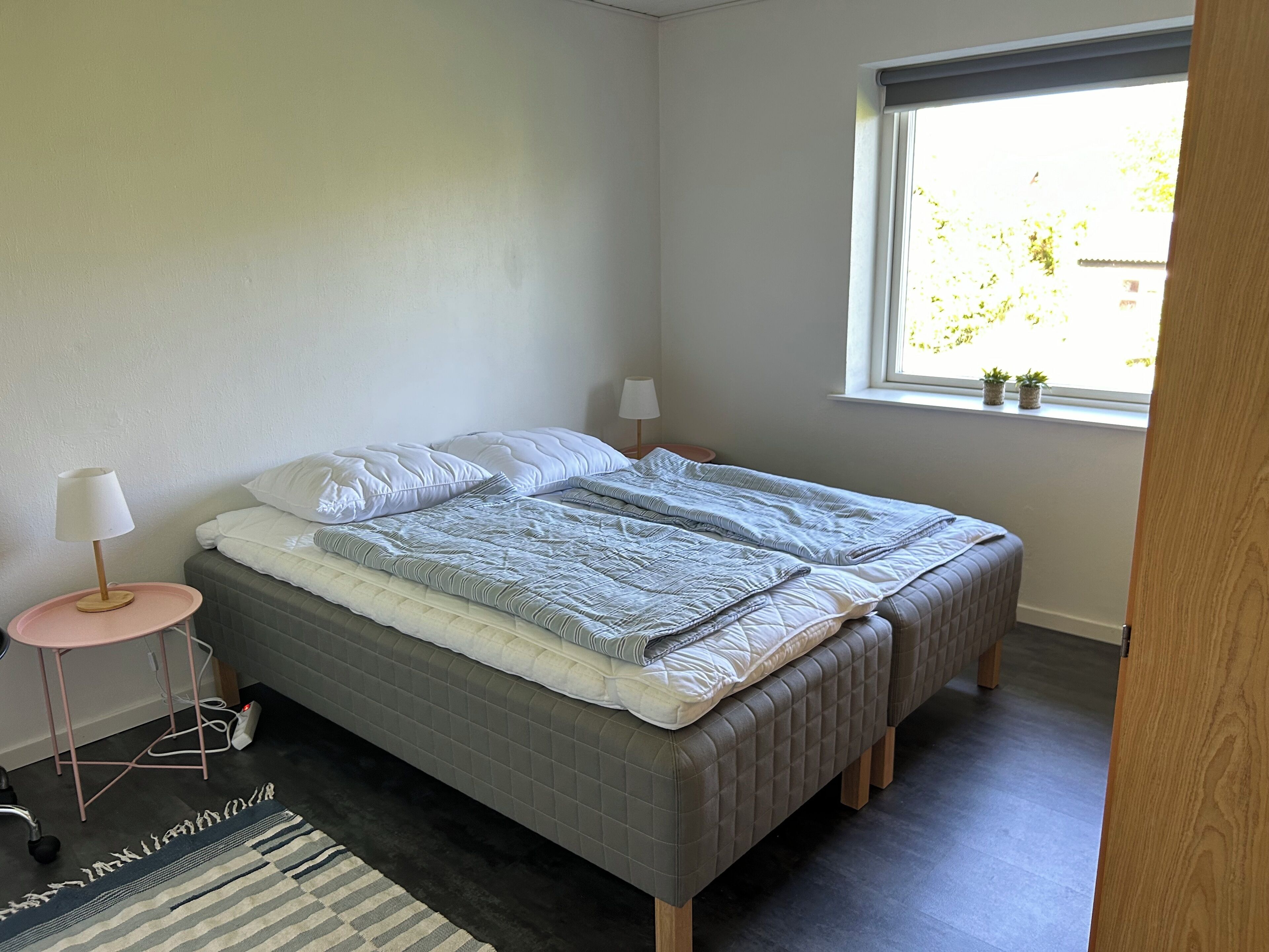 Ein Schlafzimmer mit einem Bett, Nachttischlampen, einem Fenster und einem kleinen Tisch mit Lampe.