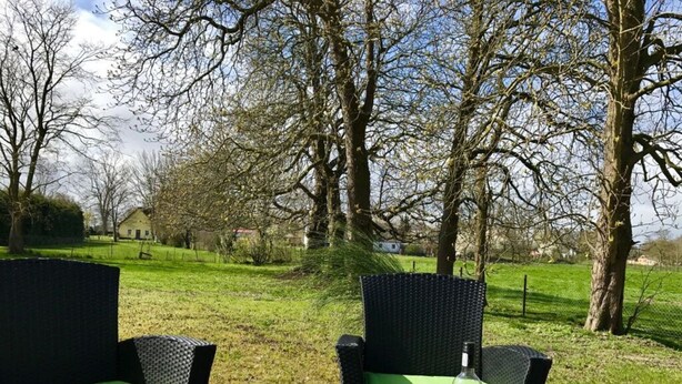 An outdoor seating area with wicker chairs and a table set for two, featuring a bottle and glasses.