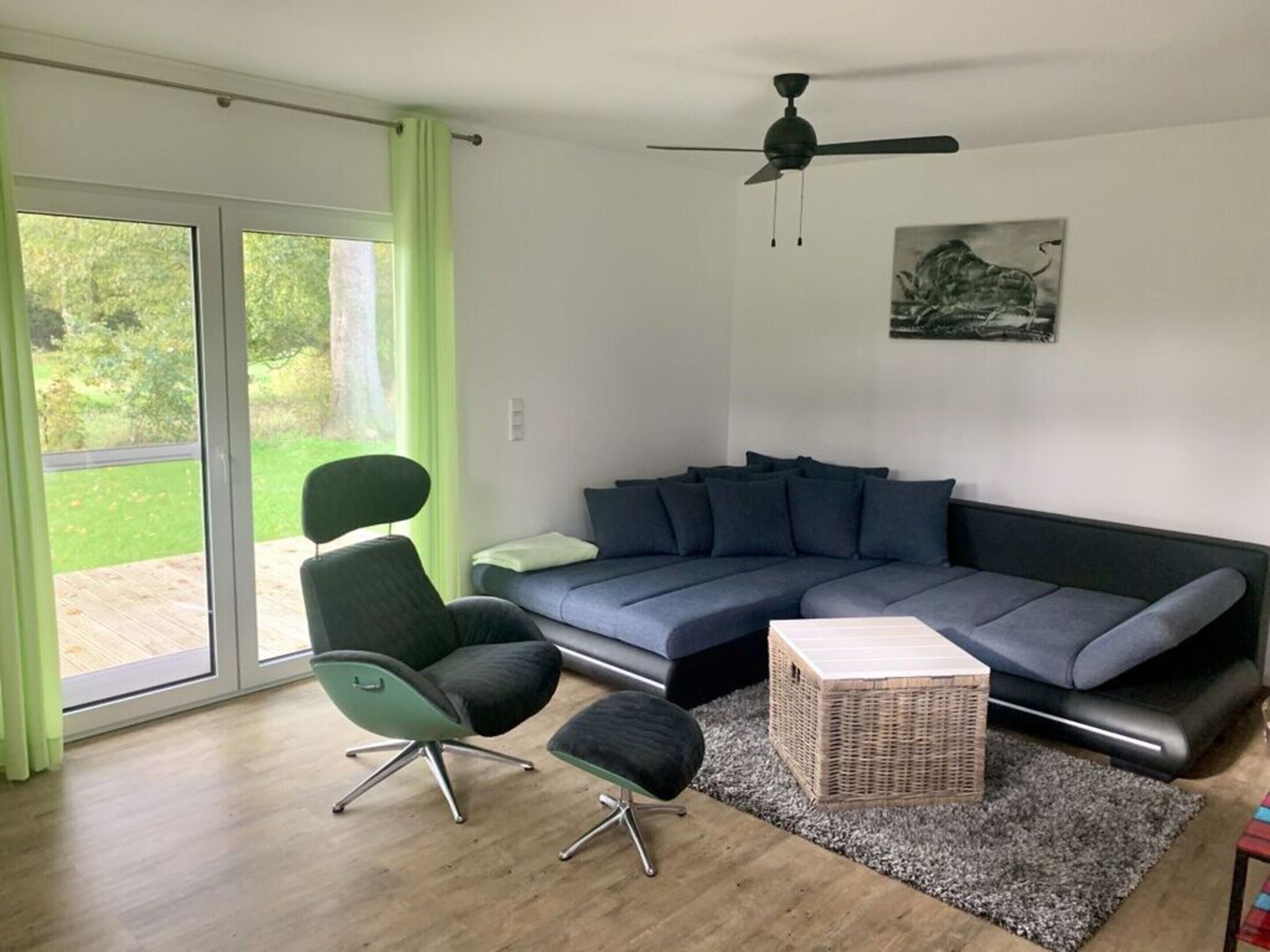 Una sala de estar moderna con un sofá seccional, un sillón verde, una mesita auxiliar y un ventilador de techo.