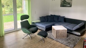 A modern living room with a sectional sofa, a green armchair, a small side table, and a ceiling fan.