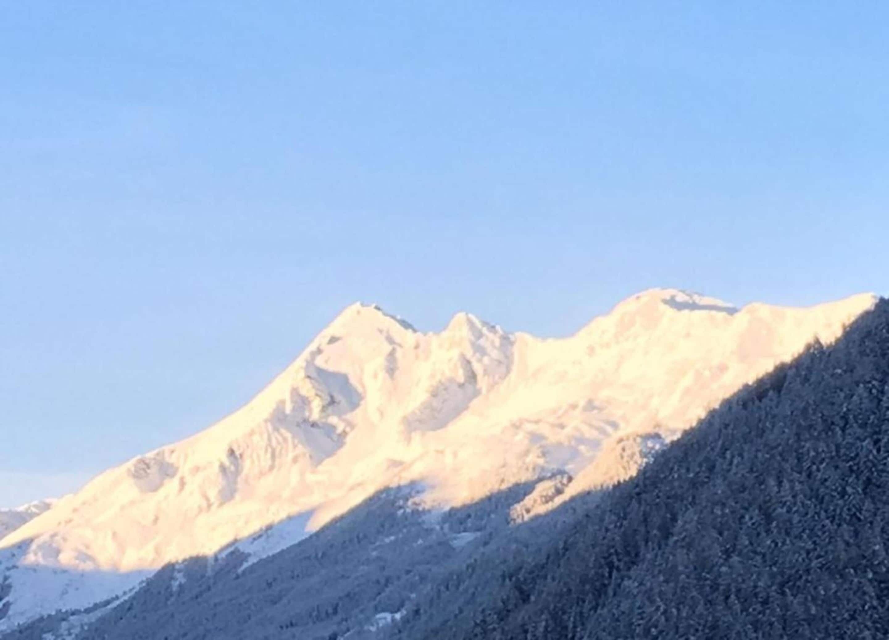 A mountain with snow-covered peaks and a forested slope.
