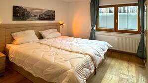 A neatly made bed with a wooden headboard, a bedside lamp, and a window with curtains.