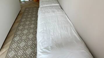 A narrow room with a patterned rug and a white bedspread.