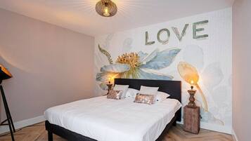 A bedroom with a bed, two bedside lamps, a wall mural with the word "LOVE" and floral designs, and a ceiling light fixture.