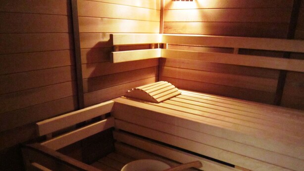 Un sauna avec des bancs en bois et un récipient en bois accompagné d’une cuillère en bois.