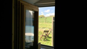 A room with a large window, a wooden door, and a view of a grassy field with a chair outside. - House Movennest (Mönchgut-Granitz)