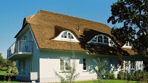 A two-story house with a thatched roof, a balcony on the upper floor, and a well-maintained lawn. - House Movennest (Mönchgut-Granitz)