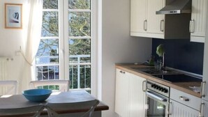 A kitchen with white cabinets, a wooden countertop, and a window with curtains. - House Movennest (Mönchgut-Granitz)