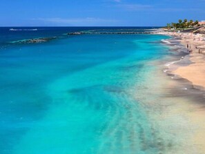 Una spiaggia con acque cristalline color turchese, una riva sabbiosa e un molo che si protende verso il mare.