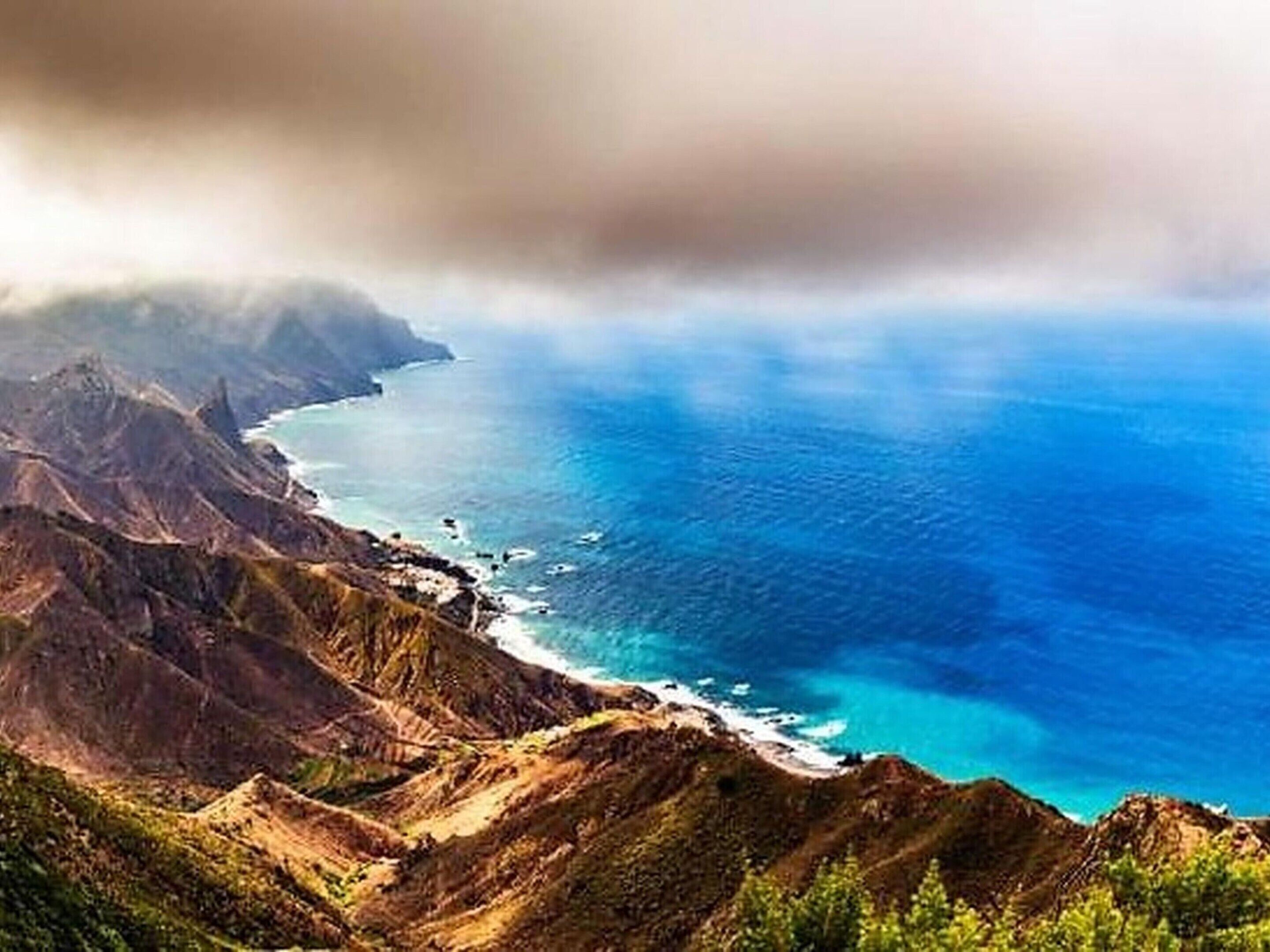 A coastal landscape with rugged terrain and a clear view of the ocean.