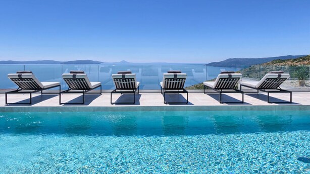 Un área junto a la piscina con sillones de descanso y una vista despejada del mar.