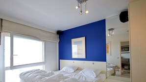 A bedroom with a bed, a dresser, a mirror, and a window. - Refined Seaview Apartment (De Haan)