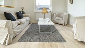 A modern living room with a white sofa, a smaller armchair, a coffee table, and a lamp. There is a window with a view of buildings outside. - 7 Person Holiday Home in Yngsjo-by Traum (Yngsjo)