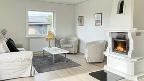 A modern living room with a fireplace, a white sofa, a coffee table, and a window with a view of a house. - 7 Person Holiday Home in Yngsjo-by Traum (Yngsjo)
