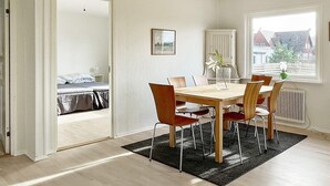 A modern room with a wooden dining table, red chairs, a black rug, a white radiator, and a window with a view of houses. - 7 Person Holiday Home in Yngsjo-by Traum (Yngsjo)