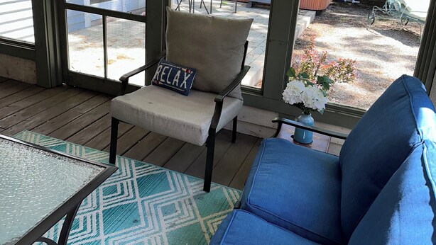 Un porche techado con una silla acolchada, un sofá azul y una mesa de vidrio.