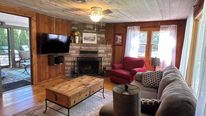 Una sala de estar acogedora con chimenea, pisos de madera, televisor y un área de estar confortable.