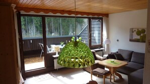 A cozy living room with a wooden ceiling, a dining area with a table and chairs, and a large window offering a view of the outdoors. - Holiday Apartment Biermann (Schluchsee)