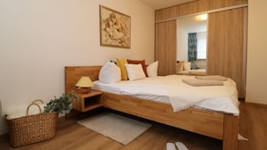 Quarto moderno com cama de madeira, mesa de cabeceira com luminária, cesto de vime e um espelho grande.