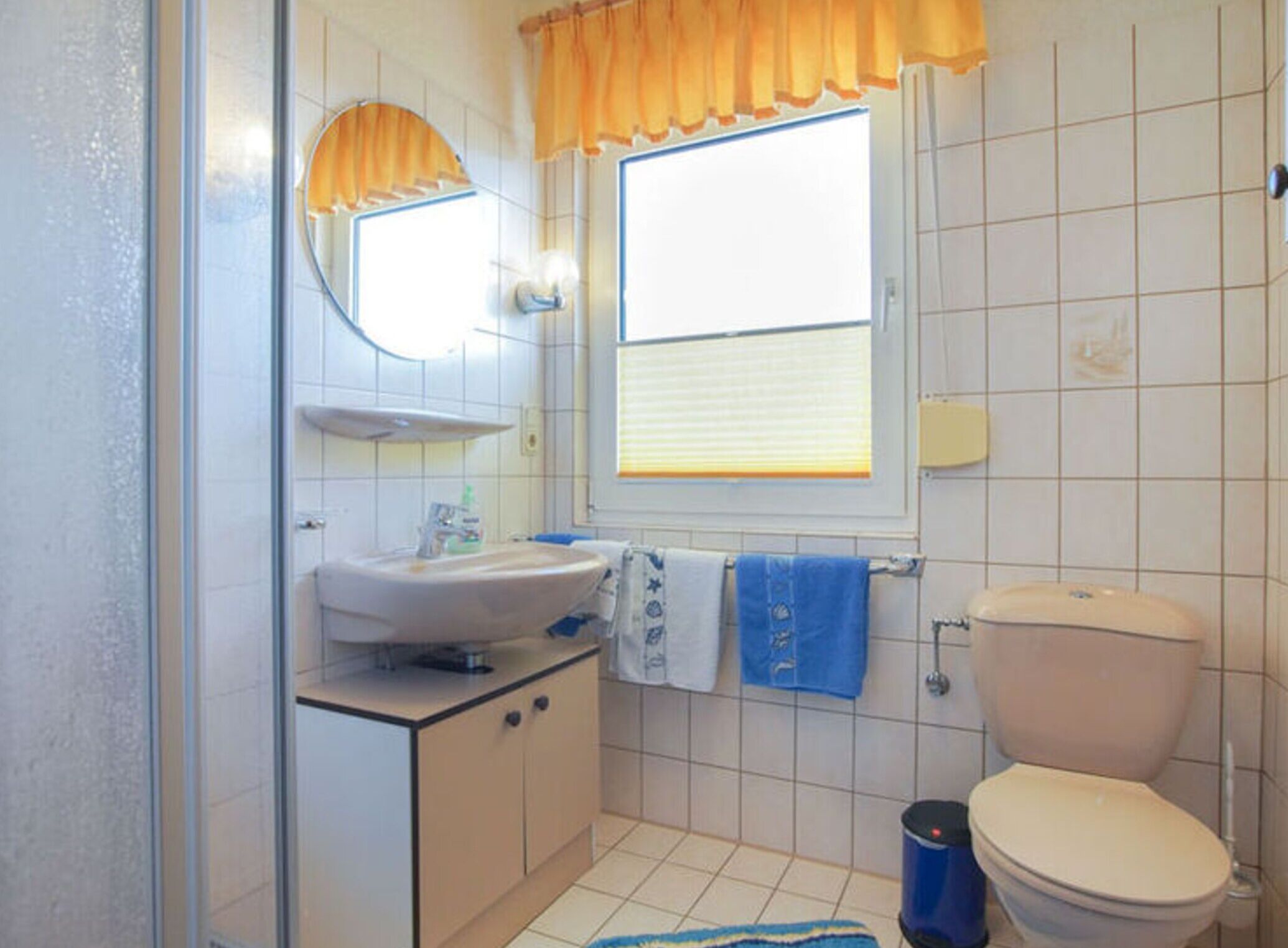 A bathroom with a toilet, sink, and a window with curtains.