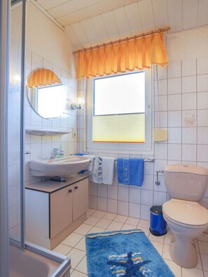 Un baño pequeño y funcional con lavamanos, espejo, inodoro y ventana con cortinas.