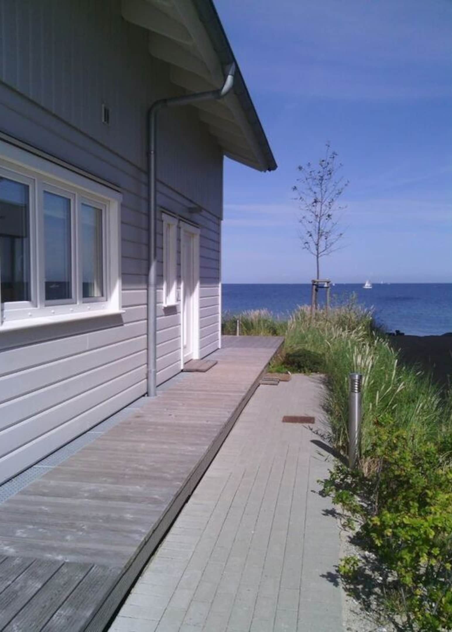 Une maison située sur la côte, dotée d’une terrasse en bois et offrant une vue sur l’océan.