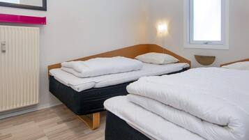 A hotel room with two beds, a radiator, a window, and a mirror.