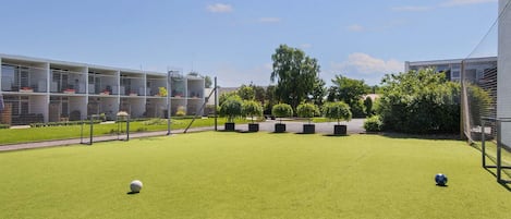 A well-maintained outdoor area with artificial grass, a soccer goal, and a building with multiple floors and balconies.