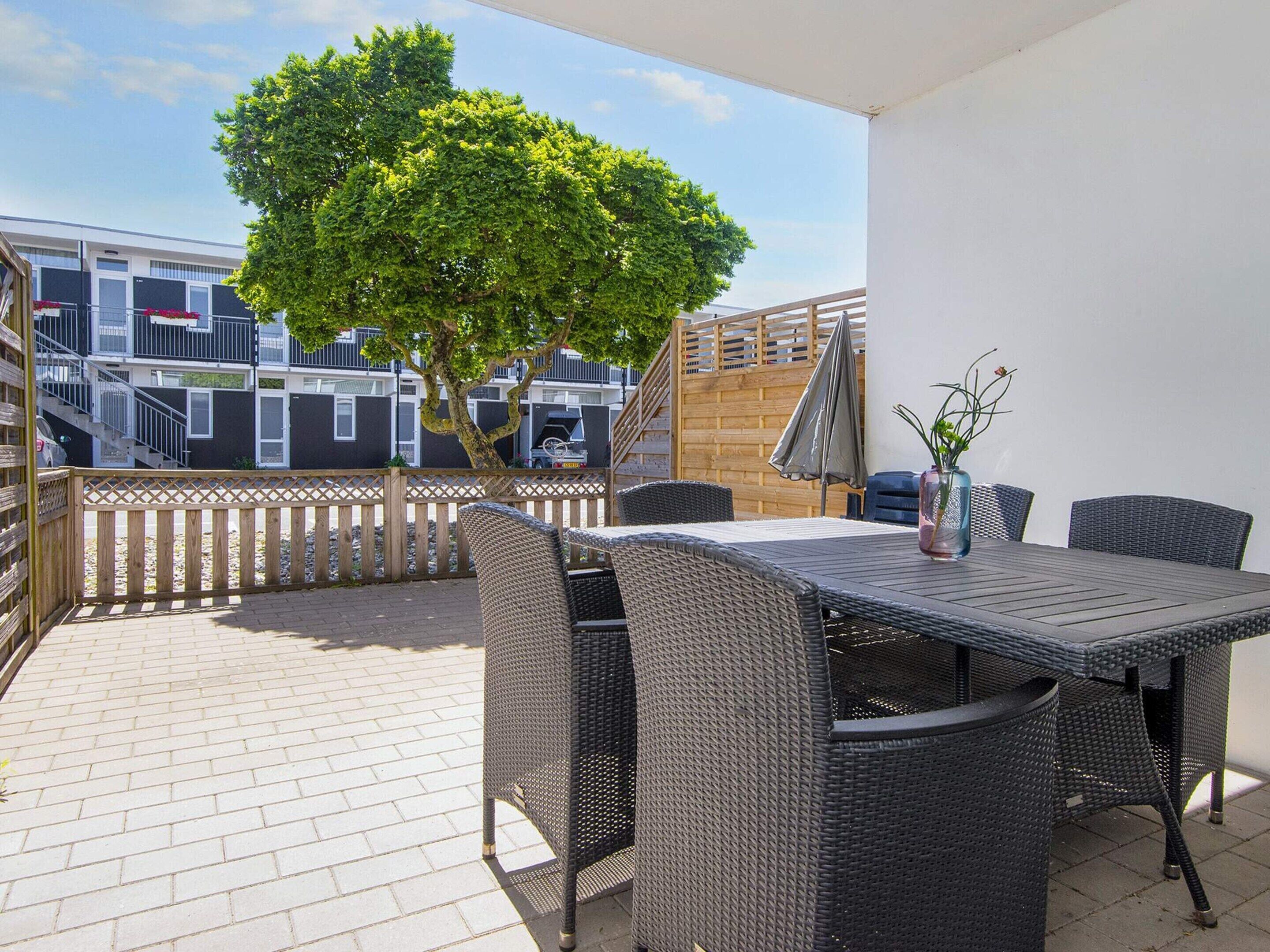 An outdoor patio with wicker furniture, a table, and a potted plant.