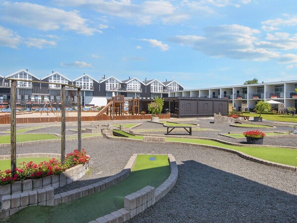 Une aire de jeux avec une structure d’escalade, une petite piscine et un espace détente comprenant une table et des chaises.