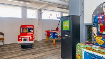 A room with a wooden floor, a red toy fire truck, a table with a colorful tablecloth, and a vending machine with a sign.