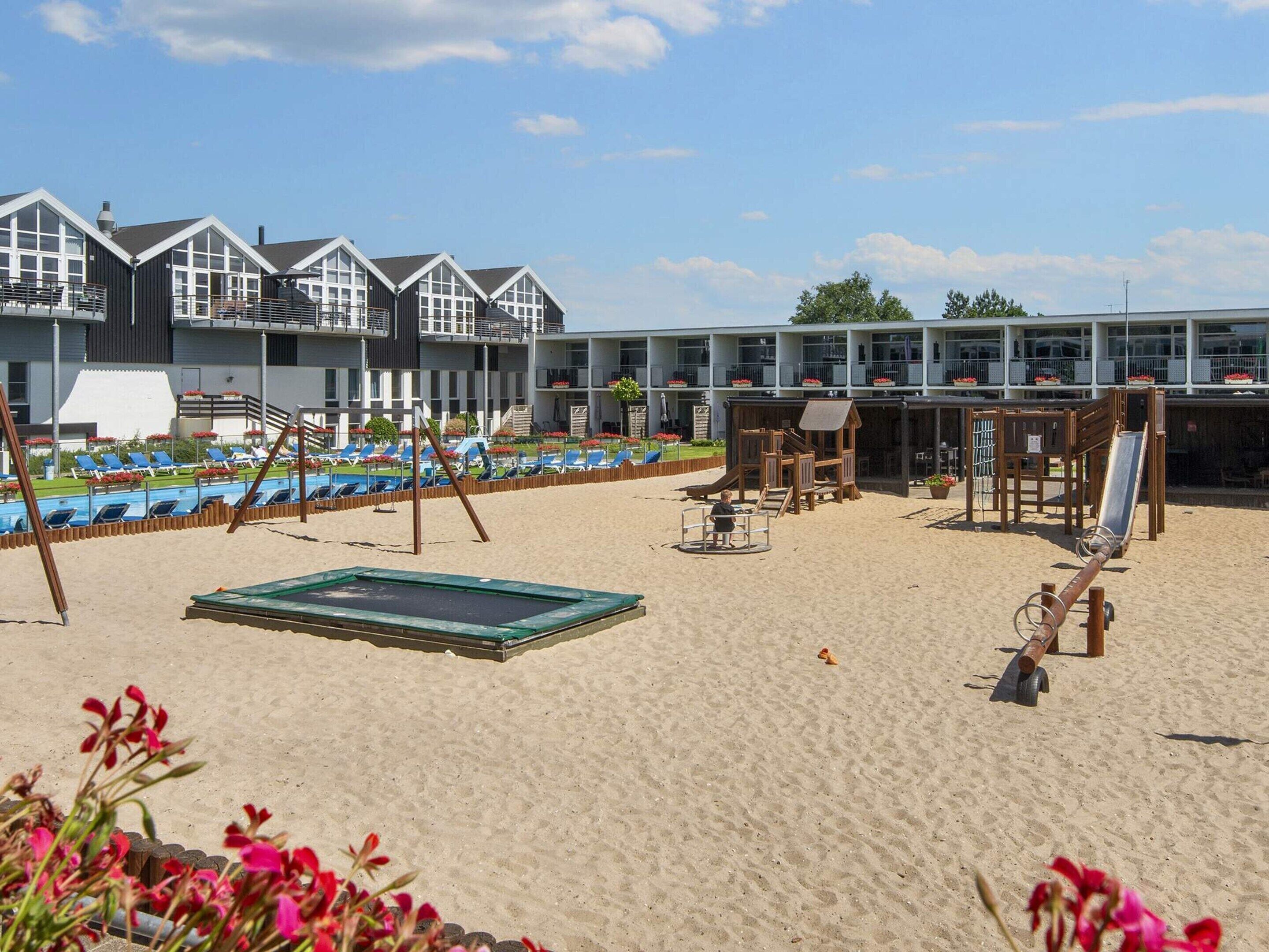 A beach area with a pool, lounge chairs, a slide, and a wooden play structure.