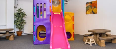 A play area with a pink slide, colorful play structures, and a potted plant.