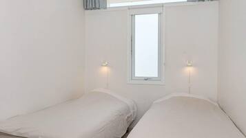 A room with two single beds, a window with curtains, and two wall-mounted reading lamps.