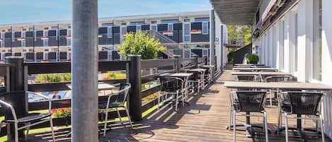 Eine Holzterrasse mit Sitzgelegenheiten im Freien und Blick auf ein Gebäude mit Balkonen.