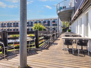 Una terraza de madera con mobiliario exterior y vistas a un edificio con balcones.