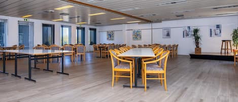 A spacious conference room with multiple tables and chairs, large windows, and artwork on the walls.
