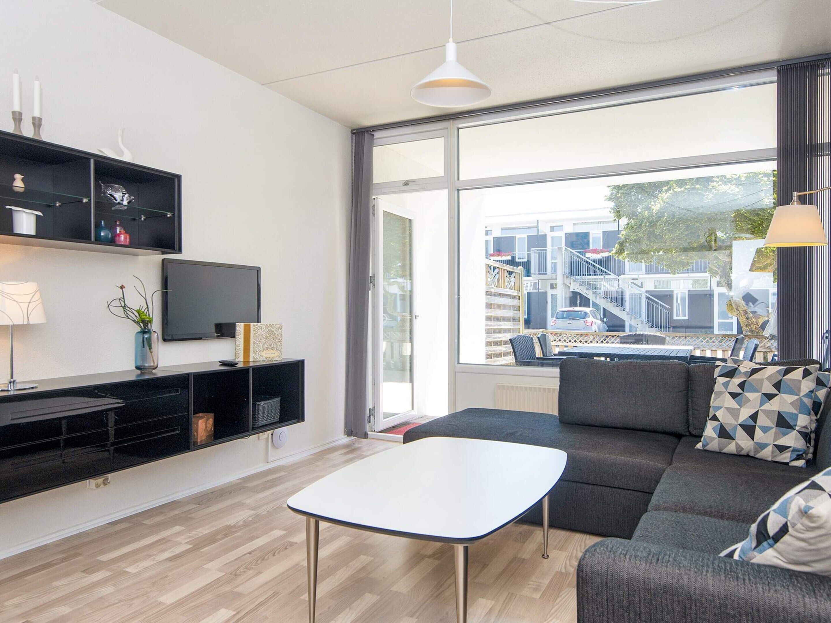 A modern living room with a sofa, a coffee table, a TV, and a large window offering a view of buildings and a car outside.