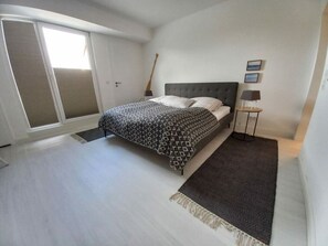 A bedroom with a bed, a nightstand, a lamp, a door with a view, and a patterned rug. - Penthouse Apartment With Pool (Groemitz)