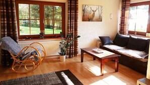 Un salon avec un plancher en bois, un fauteuil à bascule, un canapé, une table basse et une fenêtre avec des rideaux.