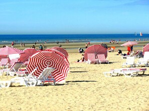 A beach with striped umbrellas and white lounge chairs. - Seagull's Nest Modern Retreat (De Panne)
