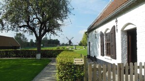 A white building with a wooden fence, a sign indicating a museum and cafe, and a windmill in the background. - Seagull's Nest Modern Retreat (De Panne)
