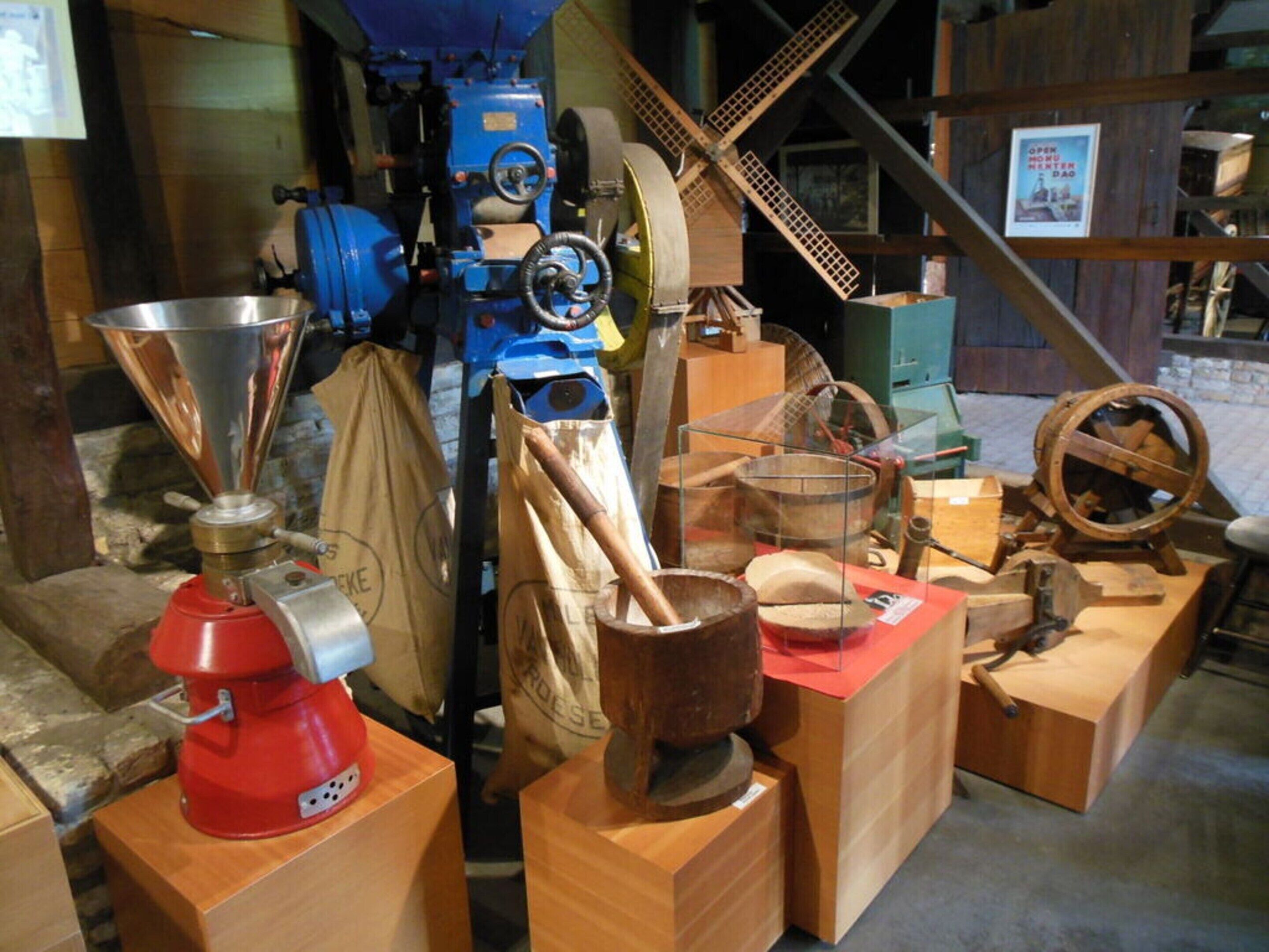 Uma exposição histórica com diversos aparelhos mecânicos, incluindo um misturador vermelho, ferramentas de madeira e uma máquina azul.