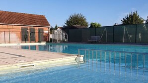 A swimming pool with a tiled deck, a fence, and a building in the background. - Seagull's Nest Modern Retreat (De Panne)